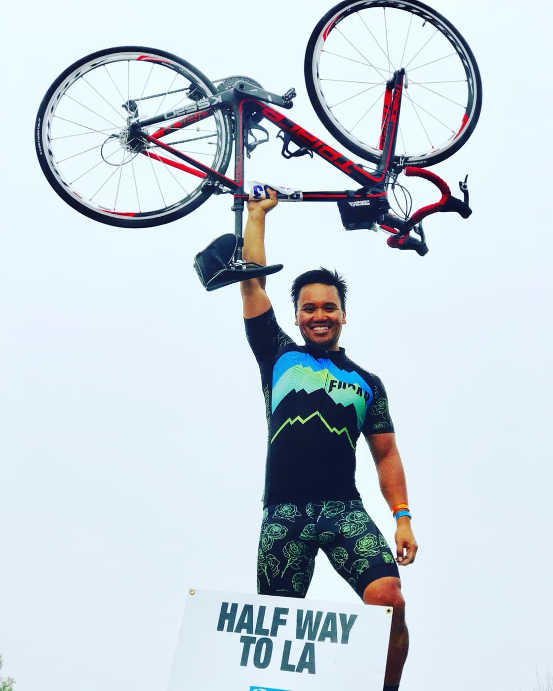 A cyclist raises a road bike overhead after an endurance event.